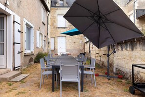 Un área de comedor al aire libre con una mesa, sillas, un paraguas grande y paredes de piedra.