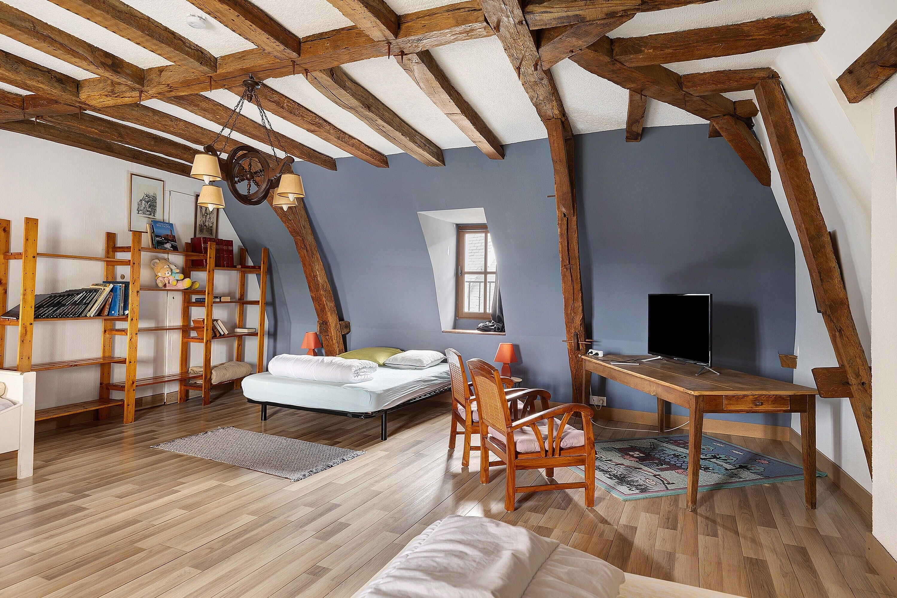 Une pièce mansardée chaleureuse avec des poutres apparentes, un lit, un bureau et un téléviseur.