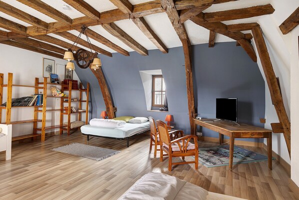 Acogedor dormitorio en ático con vigas de madera a la vista, cama, escritorio y televisor.