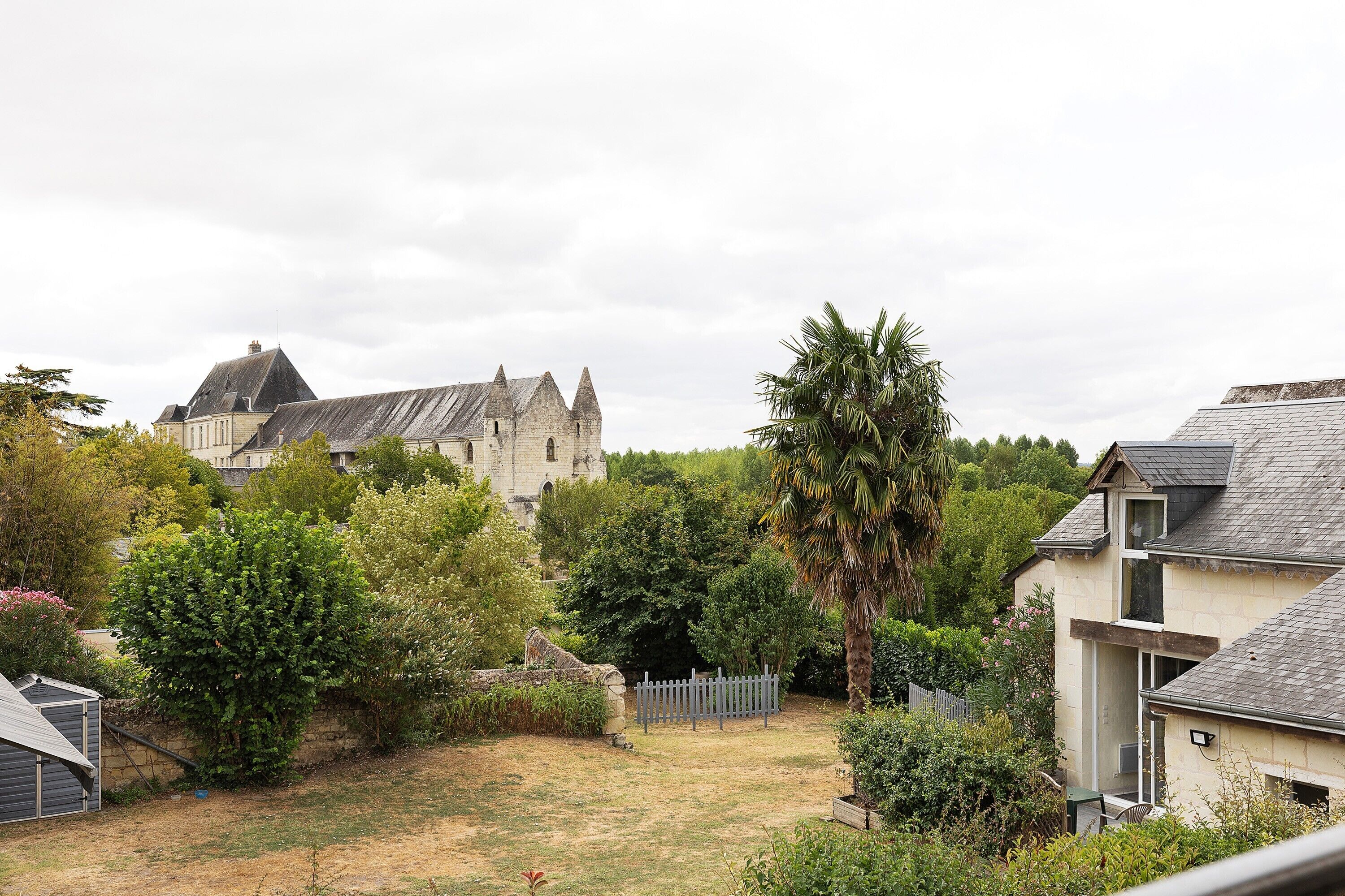 A residential area with a stone building, a fenced yard, and a variety of trees.