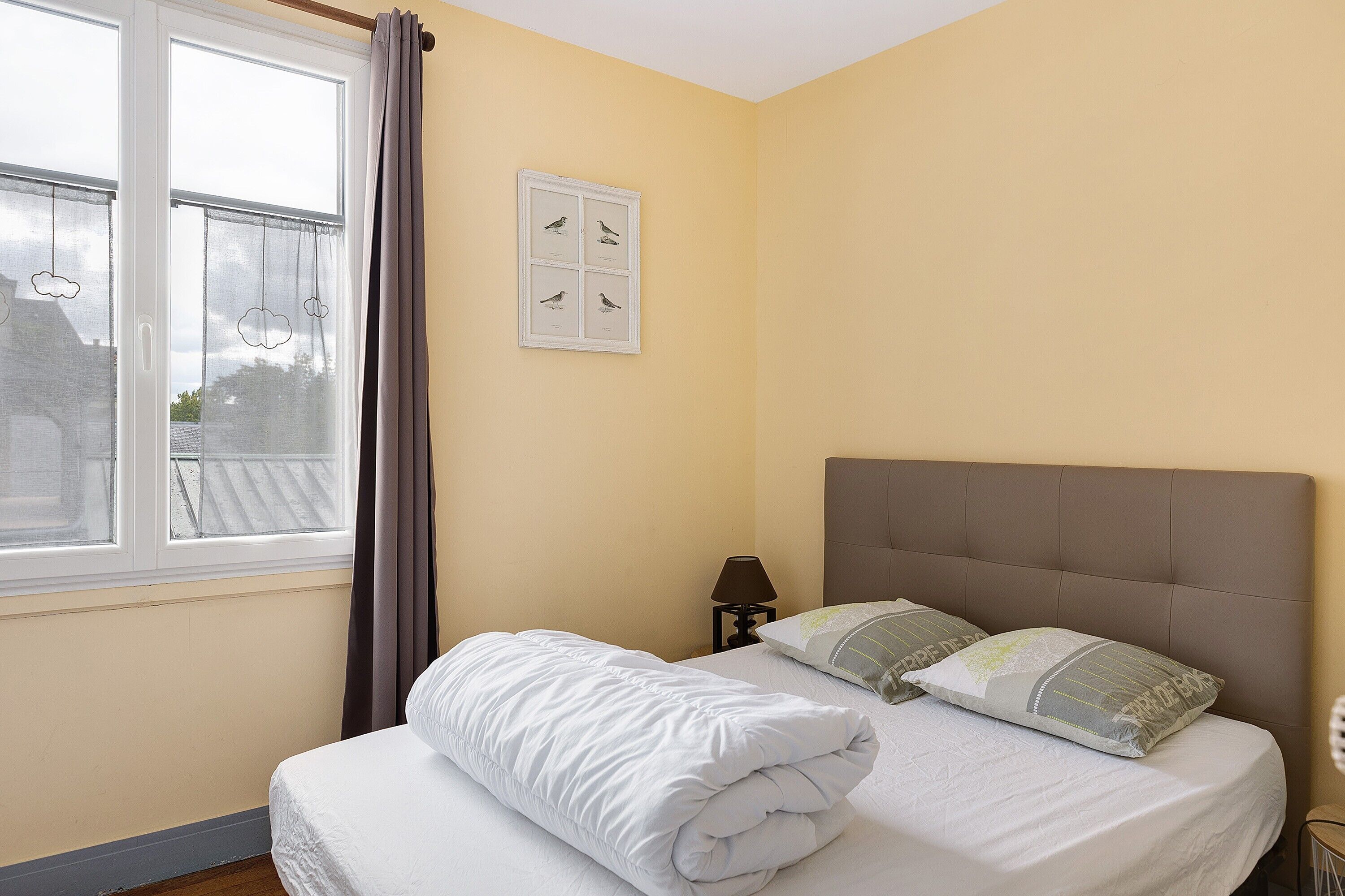 Ein Schlafzimmer mit einem Bett, einem Nachttisch, einer Lampe und einem Fenster mit Vorhängen.
