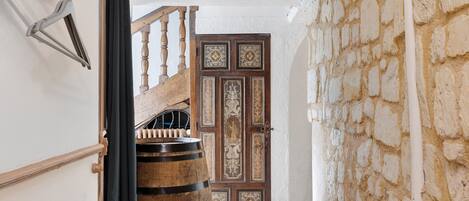Un pasillo con un barril de madera, una escalera y una puerta decorativa.