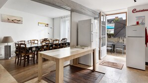 Uma sala de jantar com mesa e cadeiras de madeira, uma geladeira e vista para o exterior.