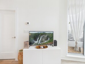 Ein Fernseher auf einer weißen Kommode mit einem Landschaftsbild, einer Fernbedienung und einem kleinen dekorativen Gegenstand auf einer Ablagefläche.