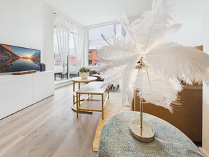 A modern living room with a large flat-screen TV, a round coffee table, a sofa, and a decorative feather lamp. - Modern Waterfront Condo with Harbour Views (Victoria Central British Columbia Provincial Government)