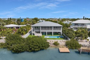 A large house with a swimming pool, surrounded by lush greenery and a body of water.