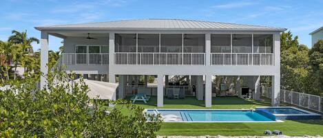 Uma casa de dois andares com piscina, área de estar coberta e quintal cercado.