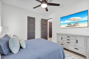 A bedroom with a bed, a ceiling fan, a TV with a beach scene, and a dresser.