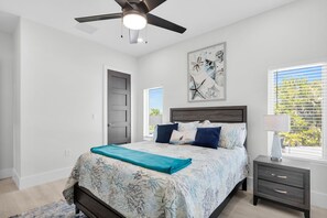 A bedroom with a bed, a nightstand, a ceiling fan, a door, and a window with blinds. - Treasure Cove- Stunning 5-bedroom, Pool Home-Walking distance to Sombraro Beach (Marathon)