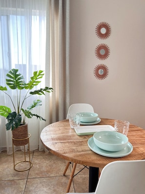 A dining area with a round wooden table, white chairs, a potted plant, and decorative wall art. - Caribbean Oasis - Bright - cozy - Close to beaches. 1-bedroom apartment with ac (Noord)