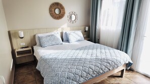 A neatly made bed with a patterned bedspread, two wall-mounted lamps, and a decorative mirror on the wall. - Caribbean Oasis - Bright - cozy - Close to beaches. 1-bedroom apartment with ac (Noord)