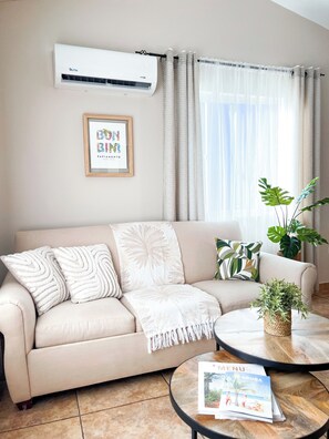 A living room with a beige sofa, a coffee table, and a magazine on it. - Caribbean Oasis - Bright - cozy - Close to beaches. 1-bedroom apartment with ac (Noord)