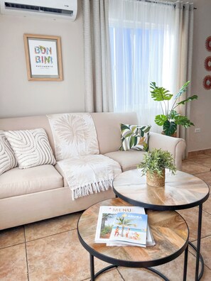 Ein Wohnzimmer mit beiger Couch, Couchtisch und Blumentopf.