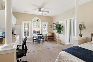 Ein geräumiges Schlafzimmer mit einem großen Bett, einem Schreibtisch und einem Stuhl. Es gibt eine Essecke mit Tisch und Stühlen sowie einen Deckenventilator.