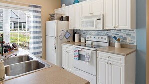 Una cocina con gabinetes blancos, estufa, microondas y refrigerador.