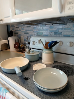 Een keuken met een witte kookplaat, een waterkoker, een broodrooster en diverse keukengerei op het aanrecht.