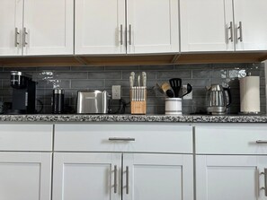 A kitchen with white cabinets, a granite countertop, and various appliances including a coffee maker, toaster, and kettle. - 2BR Stylish Home Near Short North (Columbus)