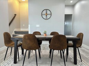 A modern dining area with a rectangular table, six chairs, a wall clock, and a staircase. - 2BR Stylish Home Near Short North (Columbus)