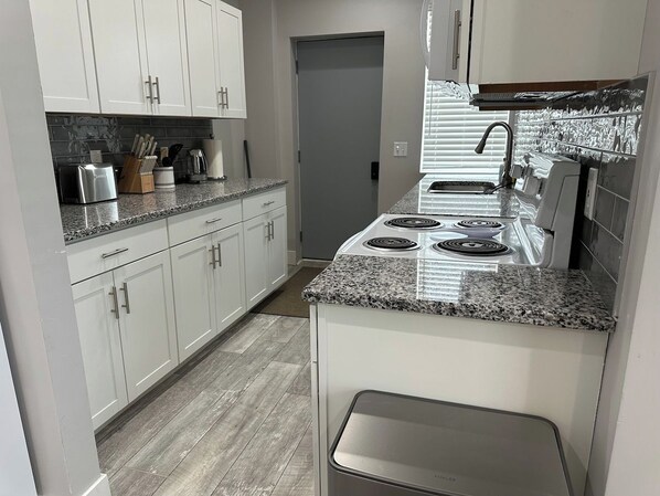 A kitchen with white cabinets, granite countertops, a built-in stove, and a microwave.