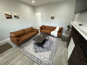 A living room with two brown leather sofas, a dark wooden coffee table, and a patterned rug. - 2BR Stylish Home Near Short North (Columbus)
