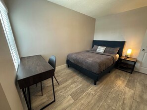 Un dormitorio con cama, mesita de noche y escritorio.