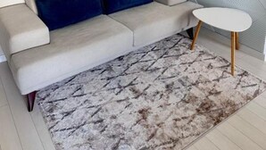 Ett modernt vardagsrum med en soffa, ett runt soffbord, en mönstrad matta och en geometrisk väggdesign.