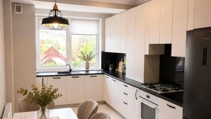 Ett modernt kök med vita skåp, ett svart kylskåp och en matplats med ett bord och stolar.