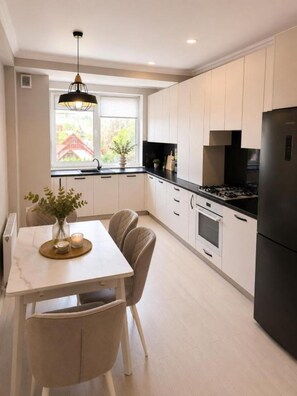 A modern kitchen with white cabinets, a black refrigerator, and a dining area with a table and chairs. - Stylish Apartment near City Center (Chișinău)