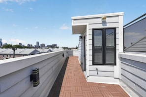 Una terraza en la azotea con vistas al horizonte de la ciudad, un área pequeña y cerrada con un ventanal, y un camino de ladrillo.