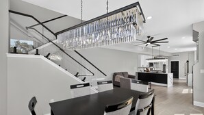 Una cucina moderna con isola centrale, una zona pranzo con tavolo nero e sedie grigie, e una scala con ringhiera in vetro.