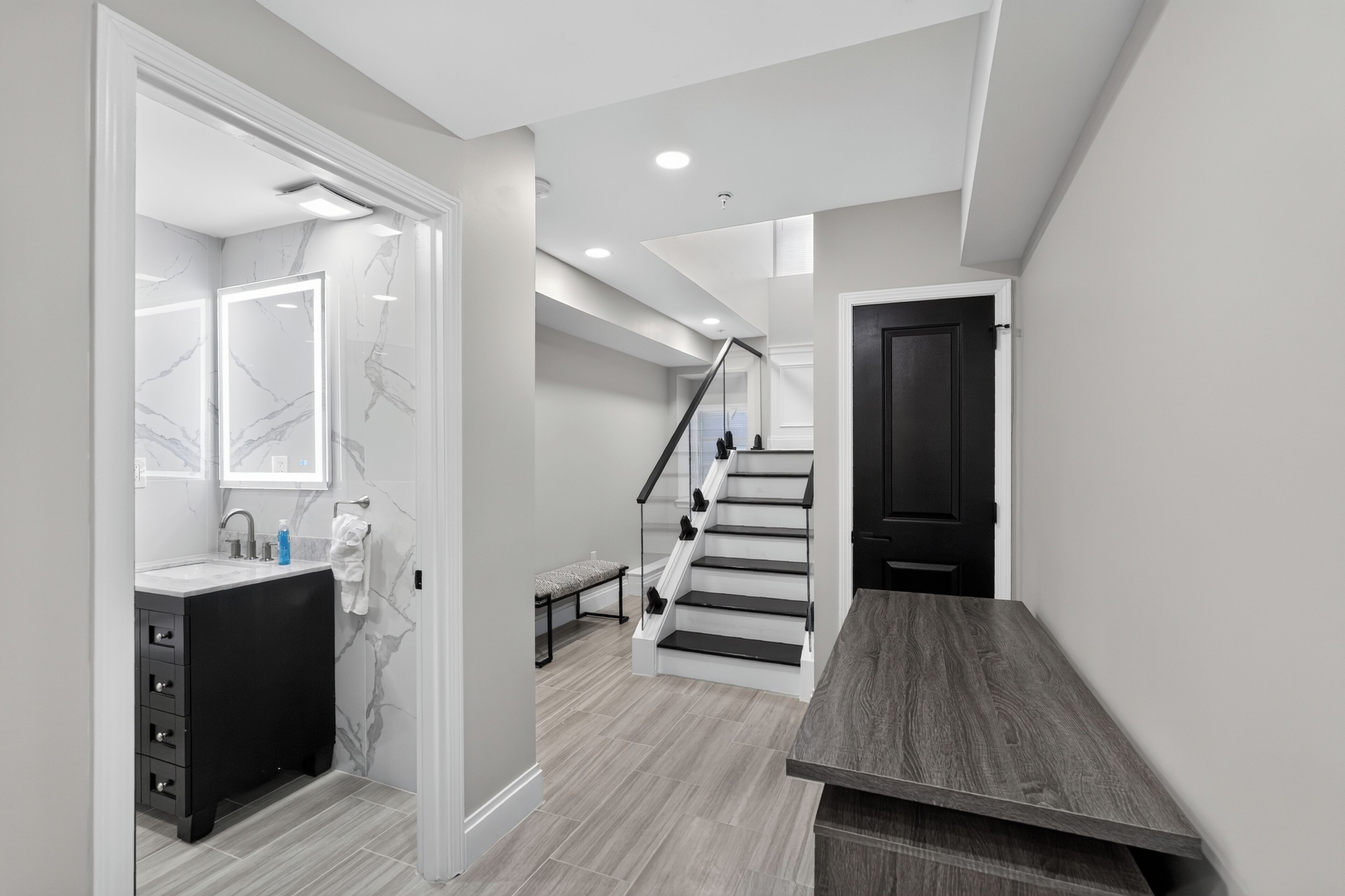A modern bathroom with a marble vanity, a mirror, and a bench.