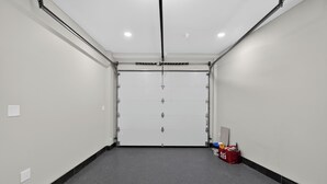 Un corridoio pulito e vuoto con un portone garage chiuso, una borsa rossa e un interruttore a muro.