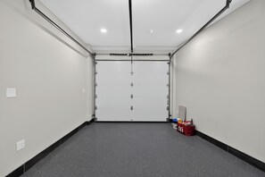 Un pasillo limpio y vacío con una puerta de garaje cerrada, un bolso rojo y un interruptor de luz en la pared.
