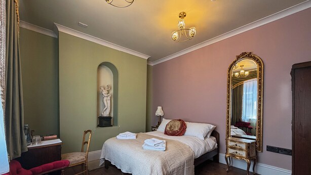 Un dormitorio con una cama, una silla, un tocador, un espejo y una estatua en la pared.
