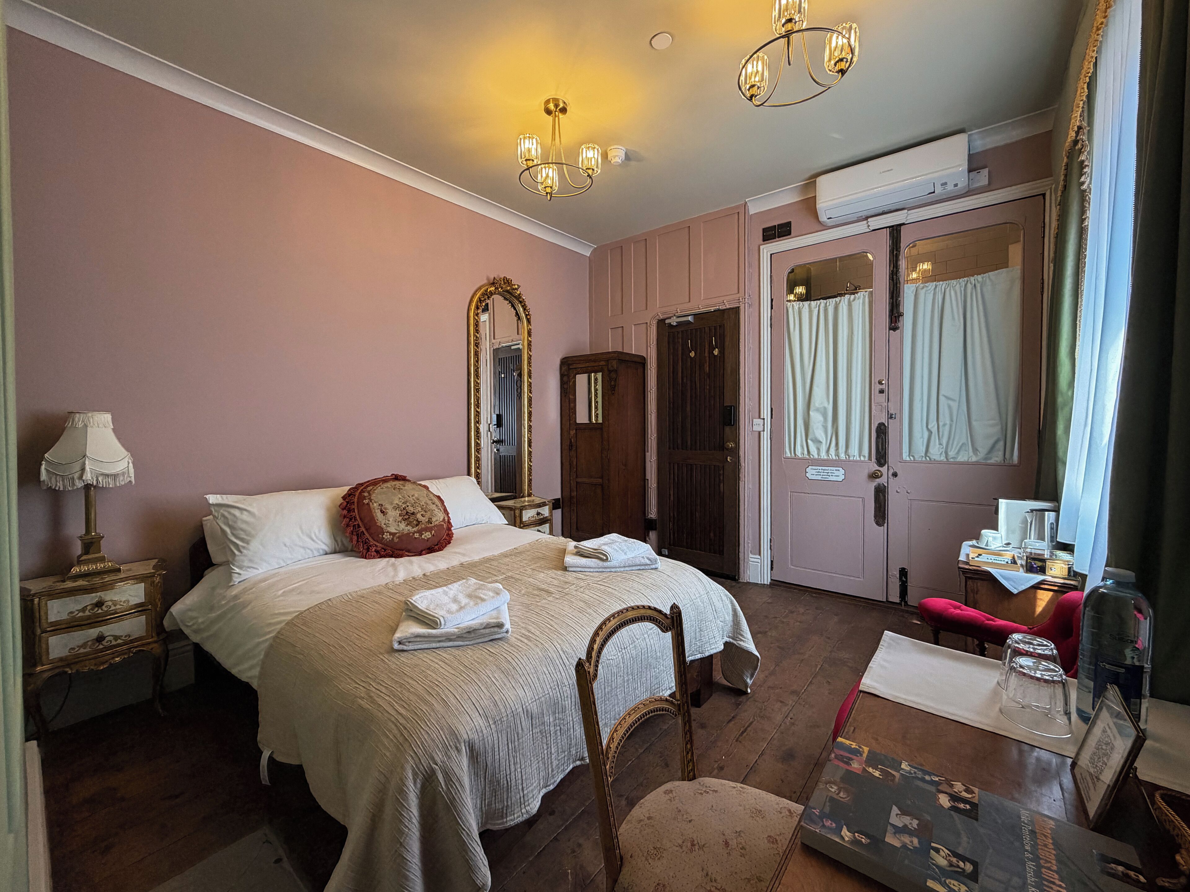 Un dormitorio con cama, espejo, cómoda, silla y una mesa con marco de fotografía.