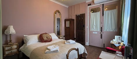 Une chambre à coucher comprenant un lit, un miroir, une commode, une chaise et une table sur laquelle est posé un cadre photo.