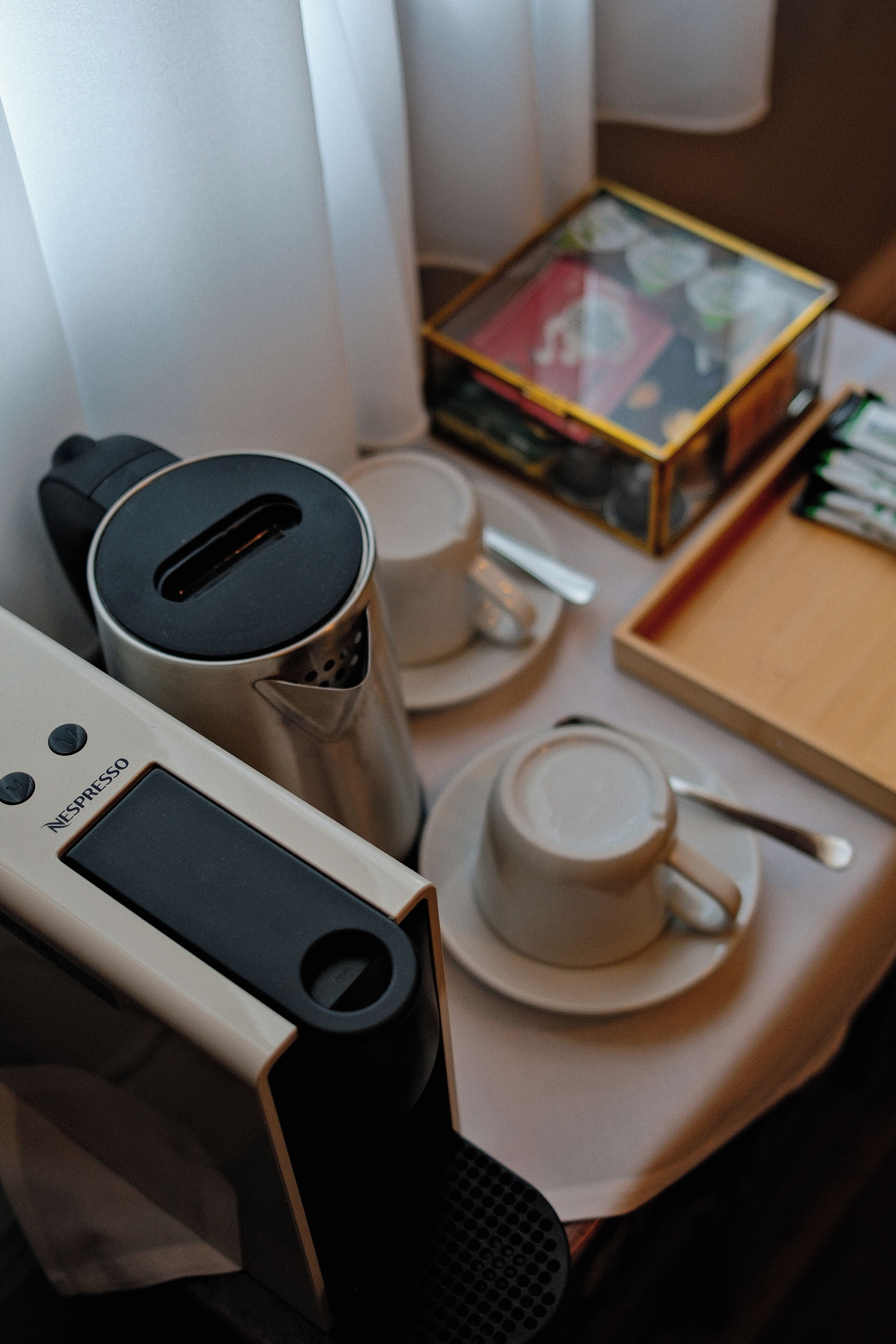 Una cafetera, tazas, una caja y una bandeja con una cuchara sobre una mesa.
