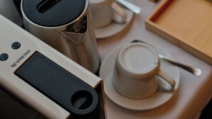 Una cafetera, tazas, una caja y una bandeja con una cuchara sobre una mesa.