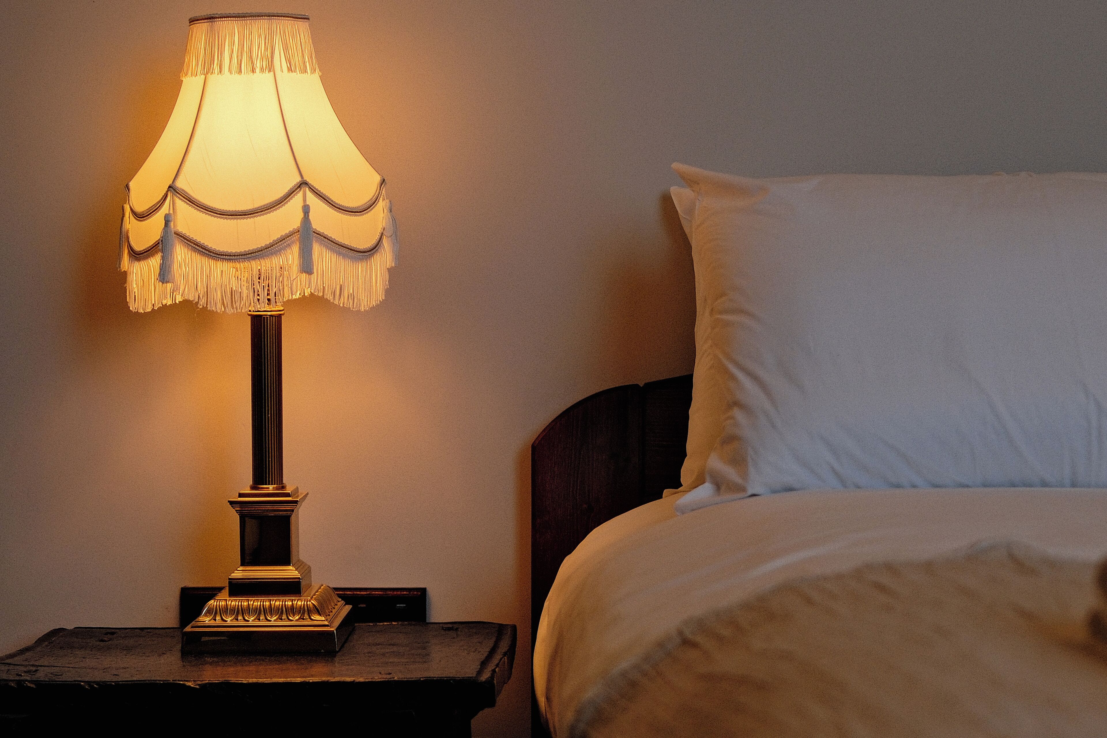 Una cama con ropa blanca y una mesita de noche con lámpara.