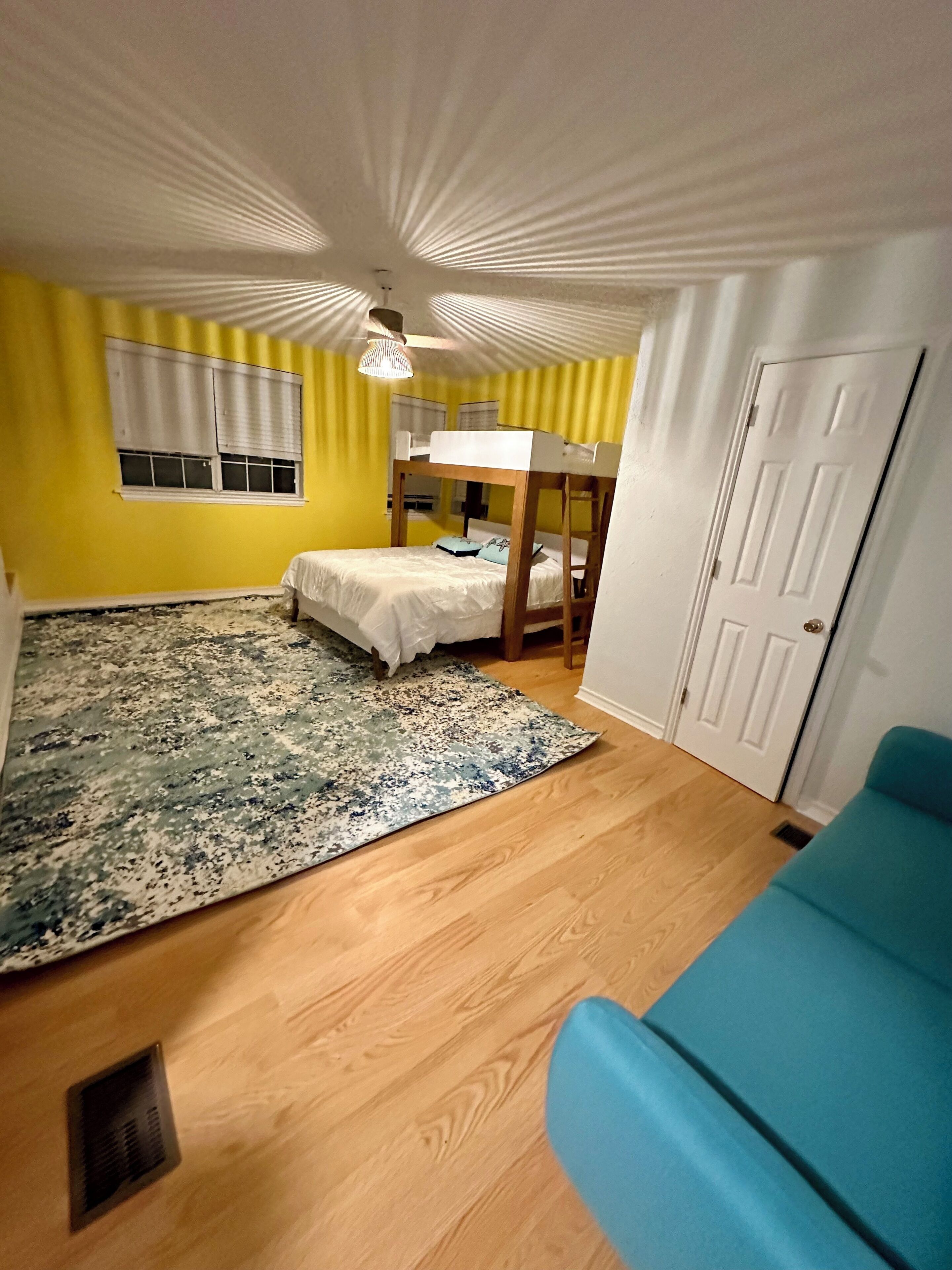 Ein Zimmer mit einem Etagenbett, einem blauen Sofa, einem gemusterten Teppich und einer weißen Tür.