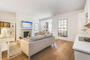 Ein modernes Wohnzimmer mit großem Flachbildfernseher, Kamin, einer Couch und einem Essbereich mit weißem Tisch und Stühlen.