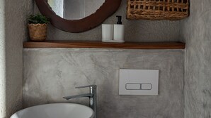 Ein Badezimmer mit einem großzügigen, weißen Waschbecken, einem runden Spiegel, einem Holzboden mit Körben und einer weißen Toilette.