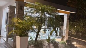 A modern building with a well-lit entrance, a large potted plant, and a paved pathway leading to the entrance.