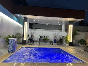 An outdoor pool area with a hot tub, seating, and potted plants.