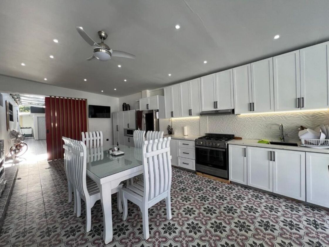 Una cocina moderna con armarios blancos, una mesa de comedor con sillas y un suelo estampado.