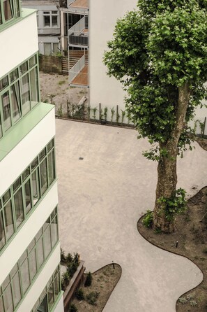 A courtyard with a large tree, a building with a balcony, and a concrete pathway. - 2BR Rooftop Terrace in Rotterdam City Centre (Rotterdam)