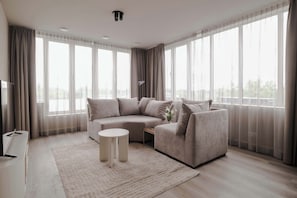 A modern living room with a sectional sofa, a small side table, and a large window with curtains. - 2BR Rooftop Terrace in Rotterdam City Centre (Rotterdam)