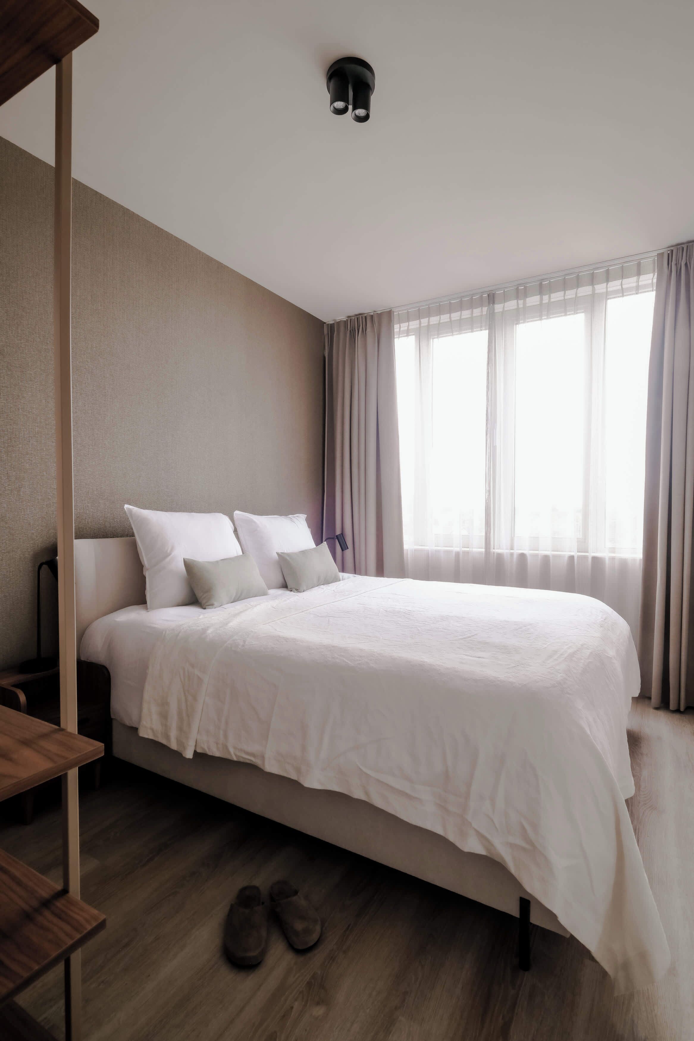A hotel room with a large bed, a wooden floor, and a window with curtains.