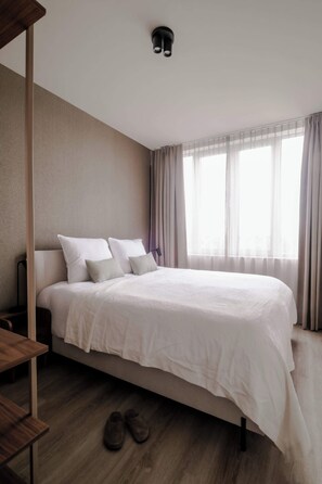 A hotel room with a large bed, a wooden floor, and a window with curtains. - 2BR Rooftop Terrace in Rotterdam City Centre (Rotterdam)