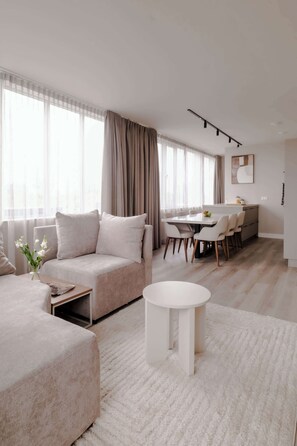 A modern living room with a sofa, a round coffee table, and a dining area with chairs and a table. - 2BR Rooftop Terrace in Rotterdam City Centre (Rotterdam)